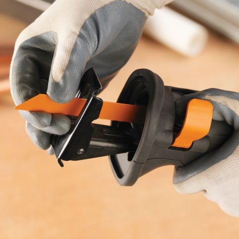En person som bär handskar med en svart och orange Evolution R230CPS Tigersåg 230V plaströrskärare för att skära igenom ett plaströr.