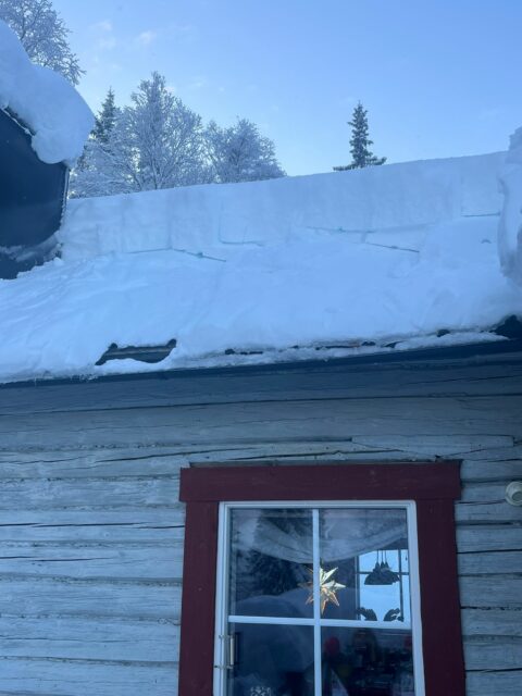 En Taksnöhyvel 5,85m med ovanligt kraftig oval alu.stång med en röd dörr delvis skymd av ett tjockt lager snö på taket och omgivande landskap.